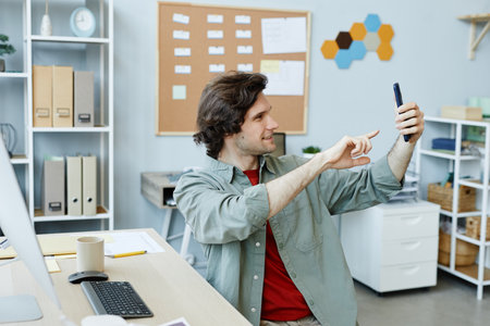 side view portrait of Caucasian young man taking selfie photo at workplace in officeの写真素材
