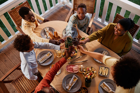 High angle view at big African American family clinking glasses over dinner table outdoors in cozy evening settingの写真素材