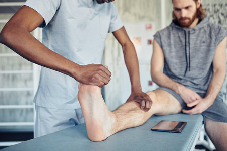 Close-up of African therapist making massage to patient on his leg while he sitting on the couchの写真素材