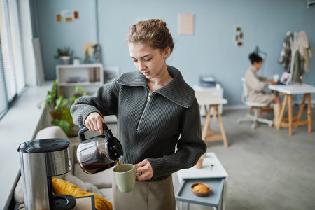 Young businesswoman pouring hot coffee in cup during coffee break at officeの写真素材