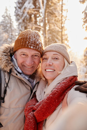 Vertical POV of happy senior couple taking selfie photo while enjoying hike in winter forestの写真素材