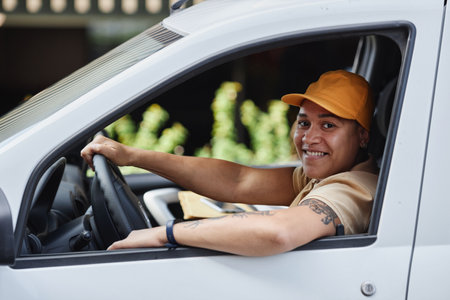 Side view portrait of female delivery worker smiling at camera from van windowの写真素材