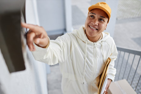 High angle portrait of smiling woman delivering packages and ringing doorbellの写真素材