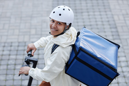 High angle portrait of smiling food delivery worker wearing helmet while riding electric scooterの写真素材
