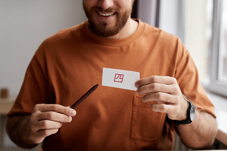 Close-up of smiling young man showing paper card with hieroglyph written with red highlighter and...
