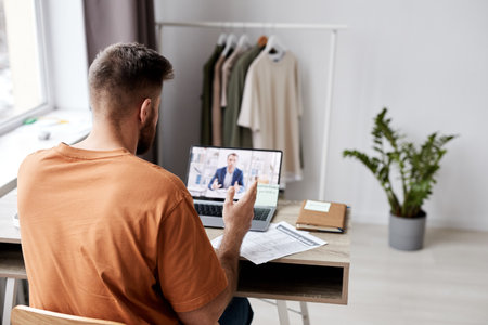 Back view of young man sitting in front of laptop with tutor on screen and asking him questions about new subject points during online lessonの写真素材
