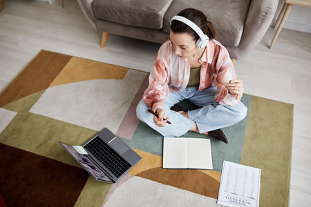 Above shot of young woman looking at laptop screen and listening to tutor explanation or answers to her questions during online lessonの写真素材