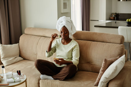 Full length portrait of young black woman watching face massage tutorial while enjoying self care day at homeの写真素材