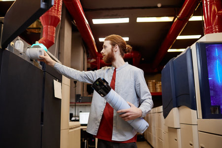 Side view portrait of young man filling ink tanks of industrial printing machine
