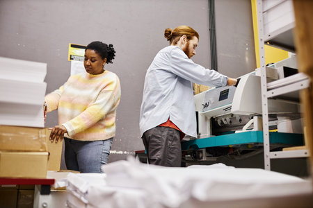 Side view of two workers operating industrial printing machine in shopの写真素材