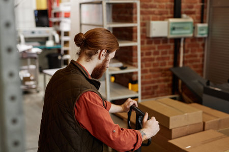 Side view portrait of male worker using pallet jack while moving boxes at printing factory warehouse