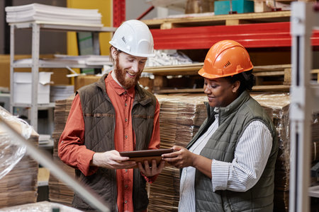 Waist up portrait of two workers wearing hardhats in factory workshop and using digital tablet