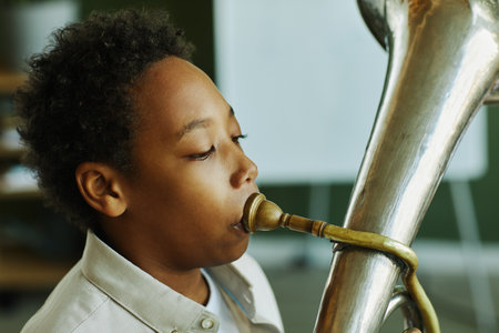 Close-up portrait of youthful African American schoolboy blowing trumpet during individual lesson of music with tutor in classroomの写真素材