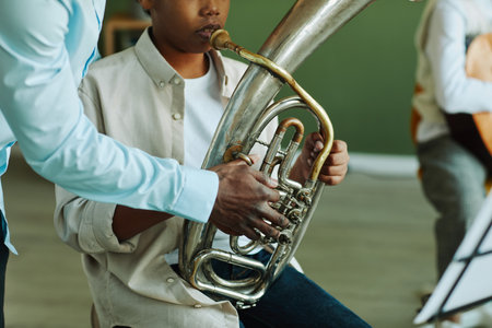 Close-up of hand of young African American music teacher helping pre-teen schoolboy with wind instrument during lessonの写真素材