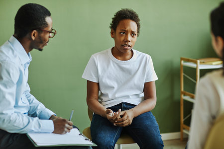Pre-teen unhappy schoolboy describing his problem to classmate while sitting in front of African...