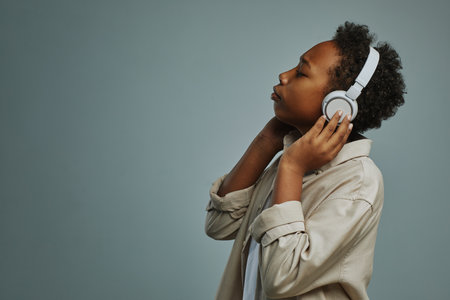 Adorable pre-teen boy in casual shirt enjoying his favorite music in headphones while posing during photo session in studioの写真素材