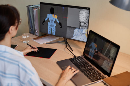 Young female designer building digital 3D models for videogame characters at workplace and using pen...