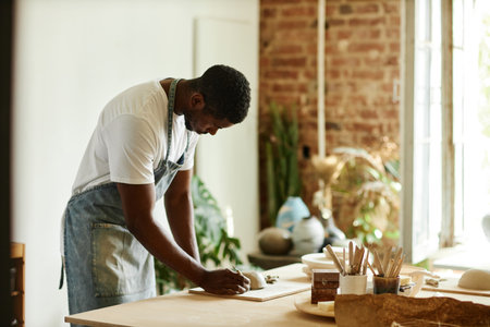 Side view portrait of young African American man creating beautiful handmade bowl in cozy pottery studio, copy spaceの写真素材