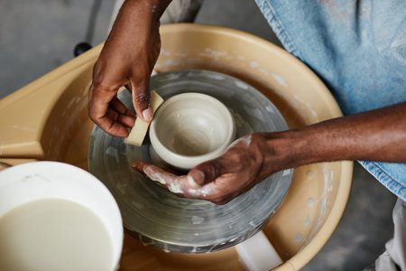 Top view of male hands of black young man using pottery wheel and creating handmade ceramicsの写真素材