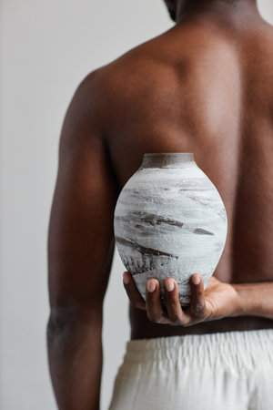 Close up of shirtless black man holding textured handmade vase behind back complementing body shape, wabi sabi designの写真素材