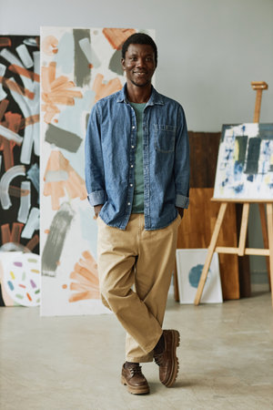 Happy young creative craftsman in casual attire standing in front of camera in studio of arts...