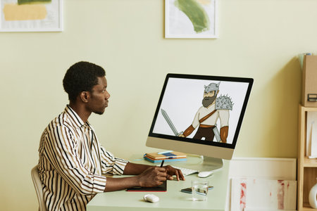 Young creative graphic designer with stylus and tablet sitting by workplace in front of computer monitor with drawn picture on screenの写真素材