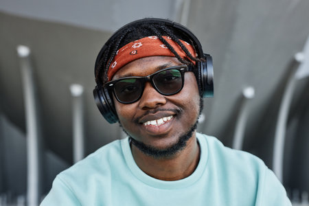 Portrait of young black man wearing headphones looking at camera outdoors and smiling