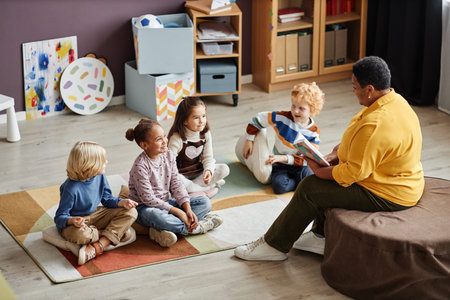 Several adorable intercultural kids gathered on the floor in front of their teacher of nursery school reading them book of talesの写真素材
