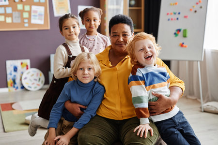 Adorable laughing boy and other intercultural little learners in casual clothes standing by their...