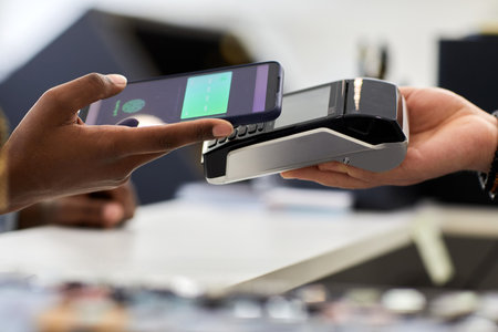 Close up of female hand holding smartphone and paying via NFC in store, copy space