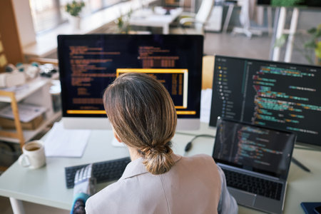 Female developer checking programming code on computer, view from backの写真素材