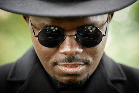 Close up of handsome African American man wearing black hat and sunglasses looking at camera...