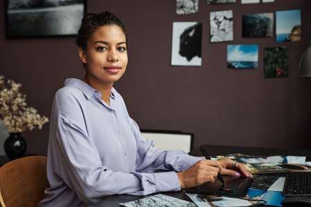Portra of posive young woman using graphic tablet when editing photos for client
