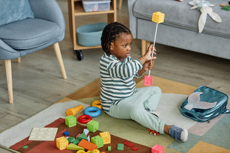 Full length portrait of cute black baby playing with toys on floor carpet in cozy home setting, copy...