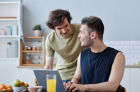 Portrait of happy same sex couple enjoying breakfast together in morning and using laptopの写真素材