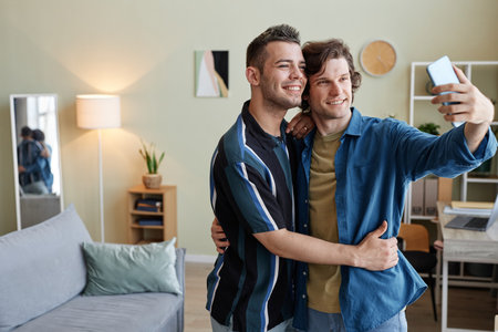 Waist up portrait of young gay couple taking selfie photo in new home together, copy space
