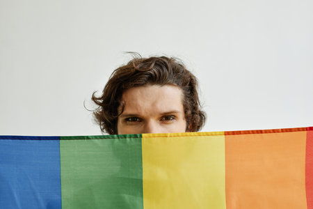 Minimal concept shot of young gay man holding pride flag, eyes visible looking at cameraの写真素材