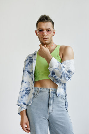 Vertical portrait of young gay man wearing extravagant outfit with crop top against white in fashion studioの写真素材