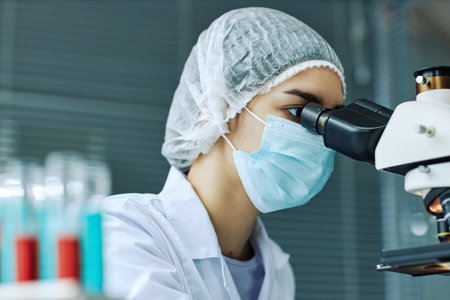Side view portrait of young woman looking in microscope while working in medical laboratory, blue tonesの写真素材