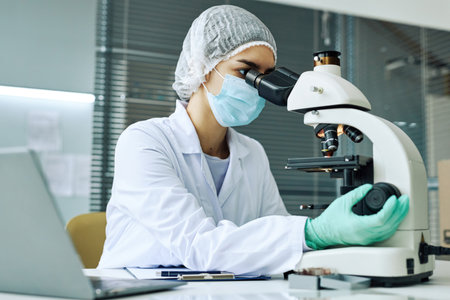 Side view portrait of young woman as female scientist working in medical laboratory and looking in...