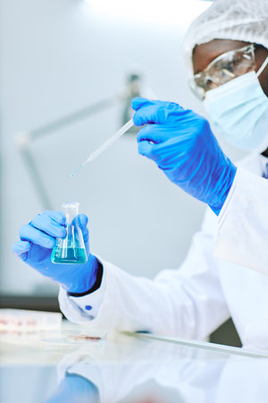 Vertical close up of African American lab technician taking liquid samples with pipette
