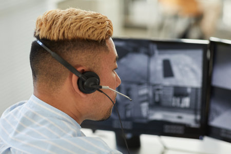 Close up of Asian man wearing headset looking at multiple surveillance feeds in monitoring and security officeの写真素材