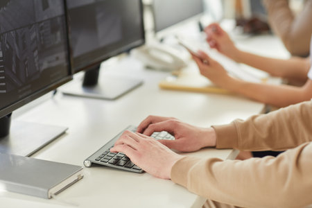 Close up of male hands typing on keyboard while using computer with surveillance camera feed in...