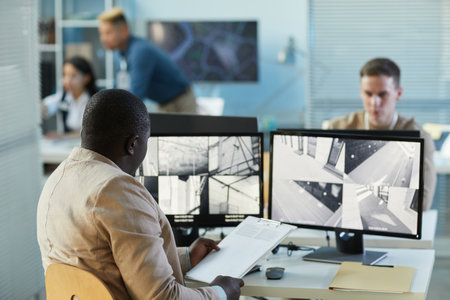 Back view of man looking at surveillance camera feeds at screen in security and monitoring center, copy spaceの写真素材