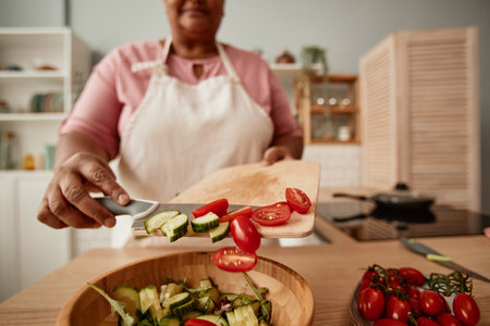Close up of black senior woman putting vegetables in bowl while making salad in kitchen, copy spaceの写真素材