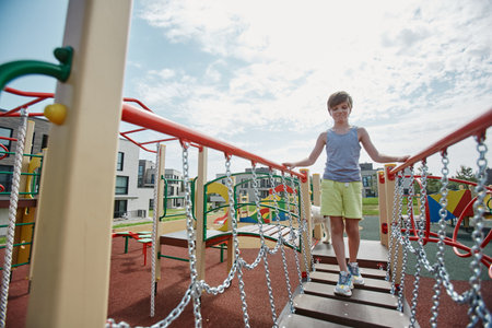 Full length portrait of young boy playing on colorful playground and walking towards camera across bridge, copy spaceの写真素材