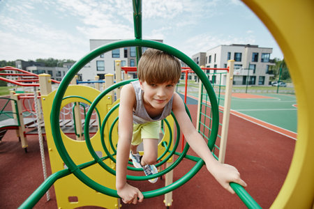 Portrait of boy playing in jungle gym on colorful playground and looking at camera, copy spaceの写真素材