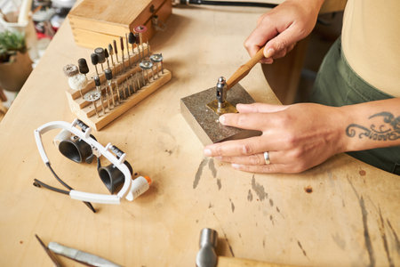 Top view closeup of tattooed female artist creating handmade jewelry ion wooden workstationの写真素材