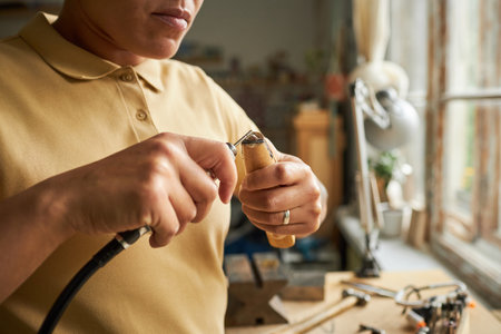 Close up of female artist creating handmade jewelry with wooden tools in cozy workshop lit by sunlight, copy spaceの写真素材