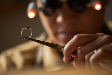 Macro shot of jeweler holding golden ring with tweezers in artisanal workshopの写真素材